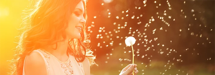Woman outdoors blowing dandelion seeds representing allergy relief through functional medicine