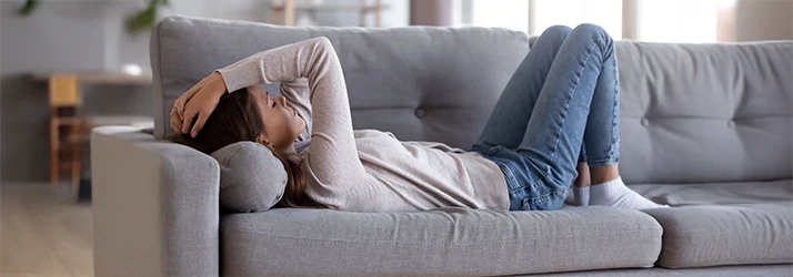 Woman experiencing chronic fatigue resting on couch, illustrating need for holistic care