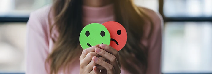 Woman holding happy and sad faces, representing mood balance from hormone therapy Woman holding happy and sad faces, representing mood balance from hormone therapy