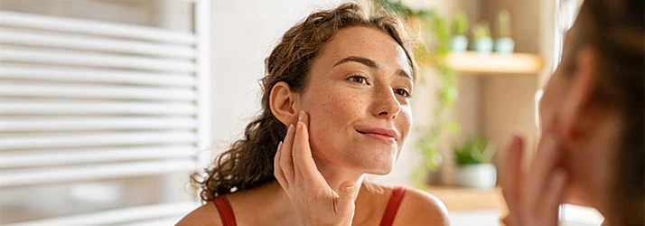Woman examining clear skin in mirror after functional medicine acne treatment